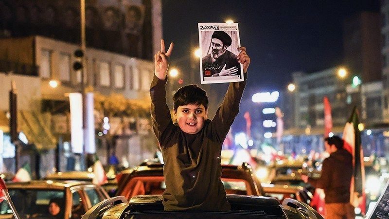 Boy holds up picture of new Supreme Leader Ayatollah Seyed Mojtaba Khamenei while raising the victory sign