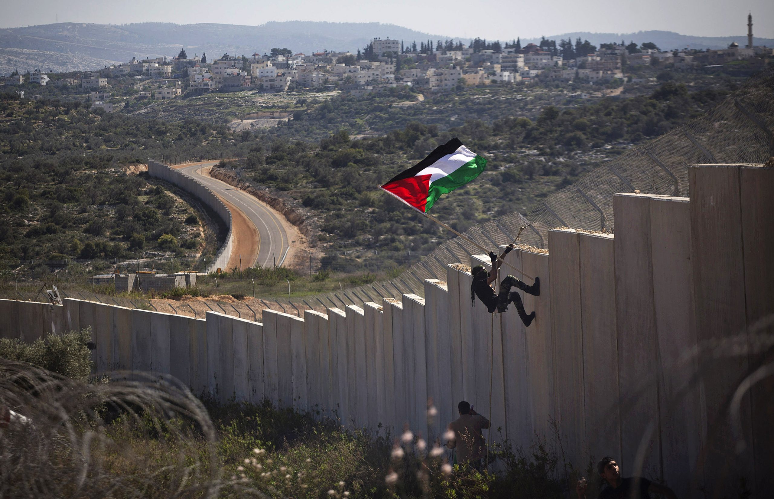 A Palestinian youth placed a flag on the Israeli Separation Wall during a protest marking nine years for the struggle against the wall in the West Bank village of Bil'in, February 28, 2014. (Photo by Oren Ziv/GroundTruth)
