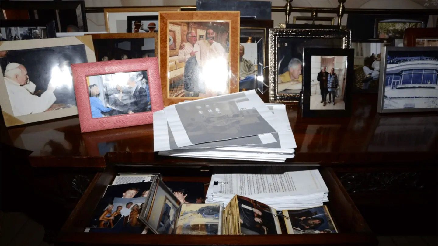 Desk drawer with printed pictures including Trump with Epstein and Ghislaine Maxwell and Trump standing with women in swimwear.