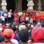 South African protestors wearing red and black raise banner against PIE amendment bill