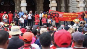 South African protestors wearing red and black raise banner against PIE amendment bill