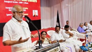 Indian left leaders speak at podium in front of red background at seminar