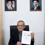 Iranian President Masoud Pezeshkian displays a document at a desk flanked by Iranian flags