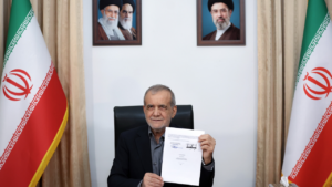 Iranian President Masoud Pezeshkian displays a document at a desk flanked by Iranian flags