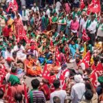 large group of Indian farmers sit in a circle holding red flags