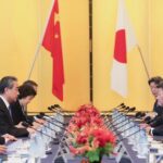 Chinese and Japanese foreign ministers sit across a table from each other with their respective flags in the background