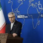 Esmail Baghaei at podium in front of blue background and flanked by Iranian flags