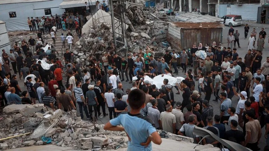 Child looks out at a crowd moving bodies in bags amidst rubble
