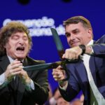 Brazilian Sen. Flavio Bolsonaro, right, handles an oversize pair of scissors, accompanied by Argentina's President Javier Milei