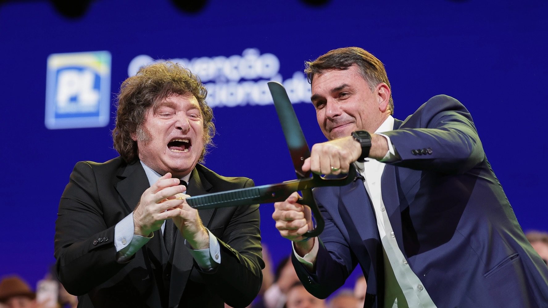 Brazilian Sen. Flavio Bolsonaro, right, handles an oversize pair of scissors, accompanied by Argentina's President Javier Milei