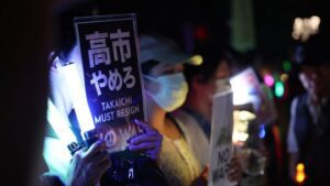 Japanese woman holds sign demanding the resignation of the prime minister.