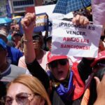 Woman holds sign that reads Down with the Sanctions! in Spanish